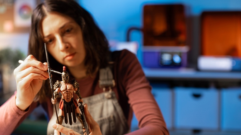 A maker painting a 3D-printed miniature, with Form Studio 1 printers in the background
